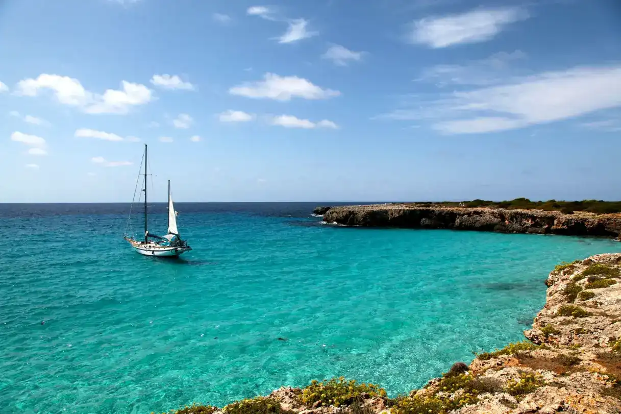 Velero navegando por las aguas turquesas de una cala en Menorca