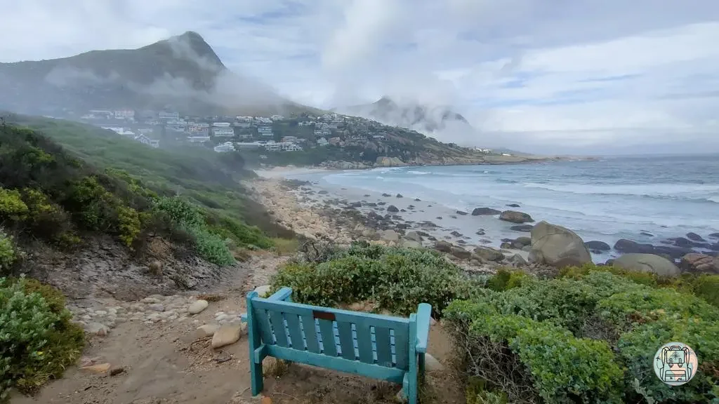 Banco azul frente a una playa costera con montañas nubladas de fondo