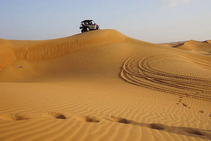 Vehículo buggy situado en la cima de una duna de arena dorada en Atlantis Dunes