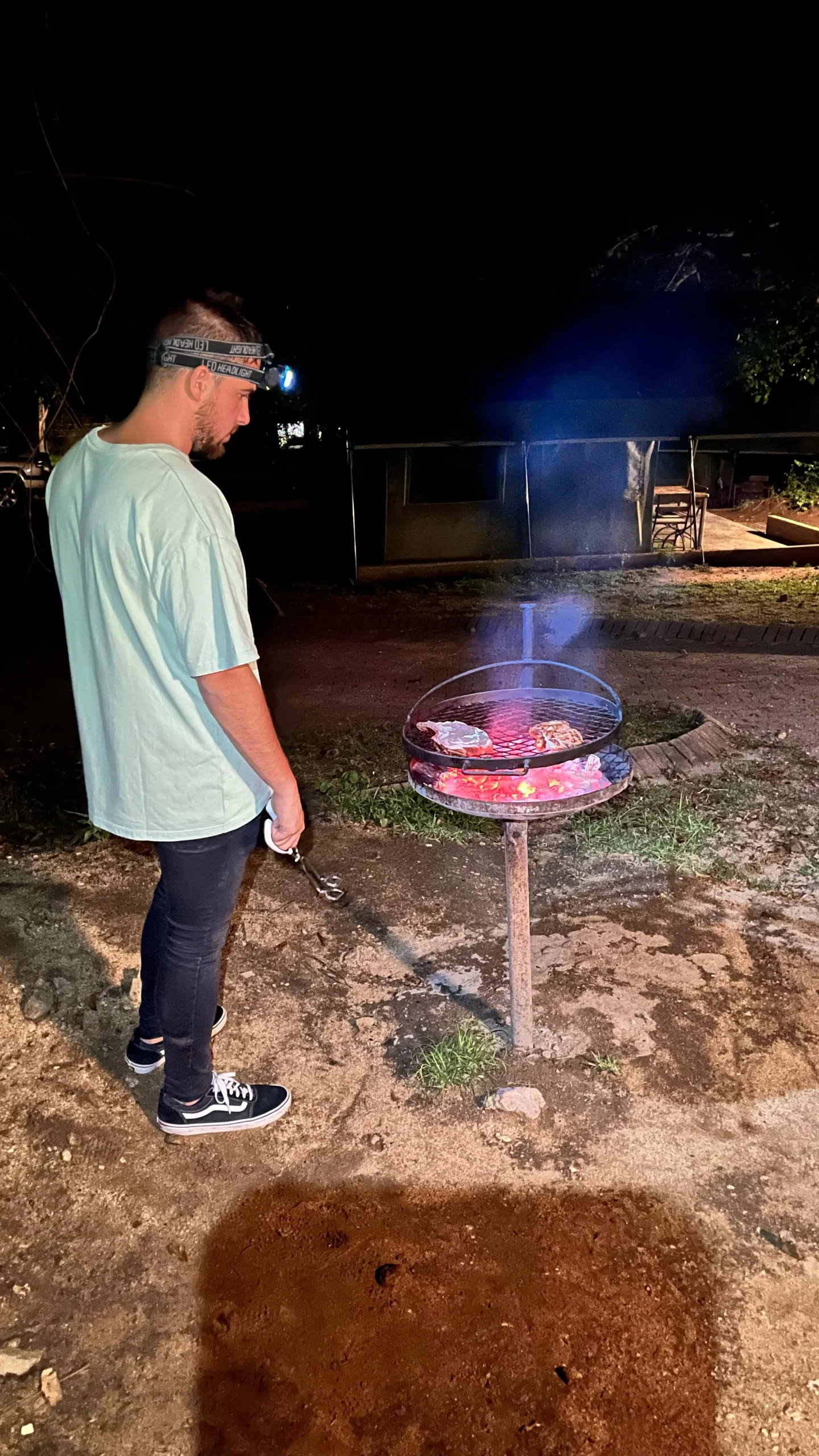 Hombre preparando una barbacoa o braai al aire libre por la noche