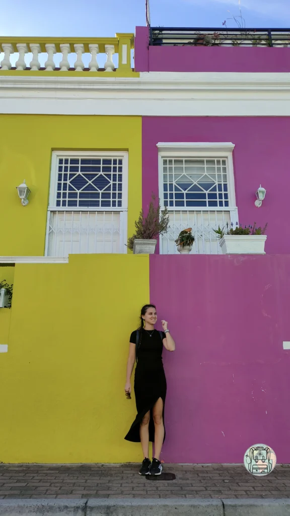 Teresa en Bo Kaap en una pared dividida en dos colores, amarillo y rosa, un sitio perfecto para incluir en nuestro blog de viajes por Ciudad del Cabo