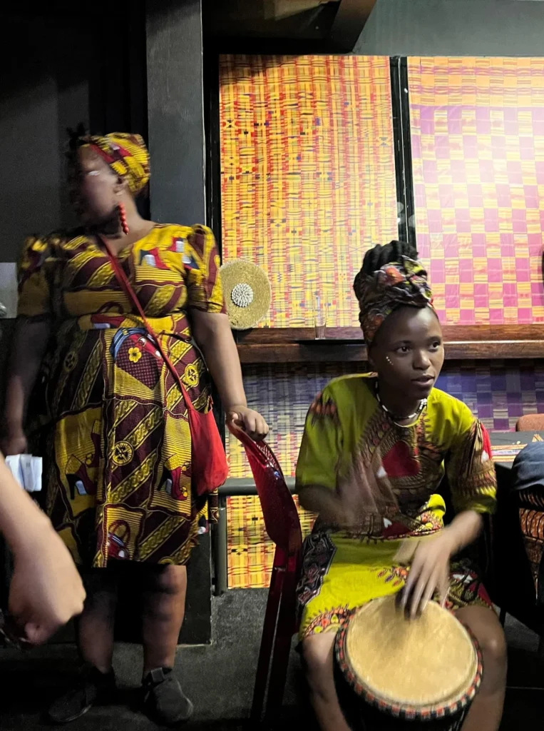 Músicos vestidos con trajes tradicionales africanos tocando el djembe en un restaurante