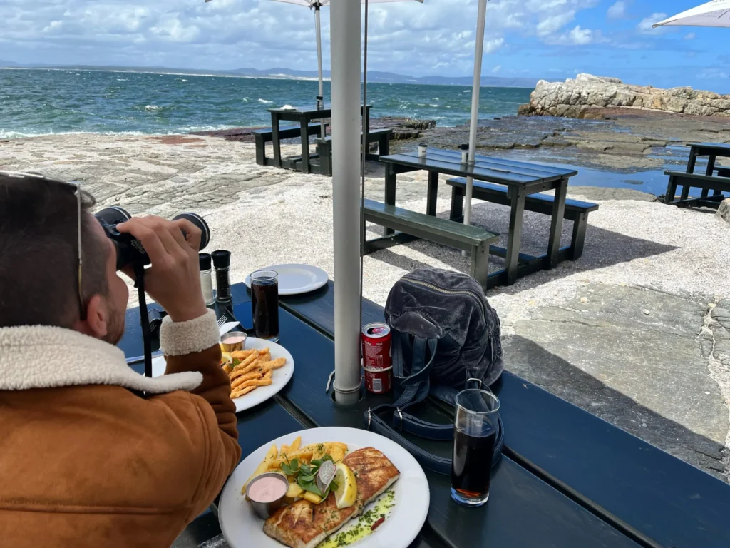 Persona mirando por prismáticos hacia el océano desde la terraza de un restaurante en Hermanus