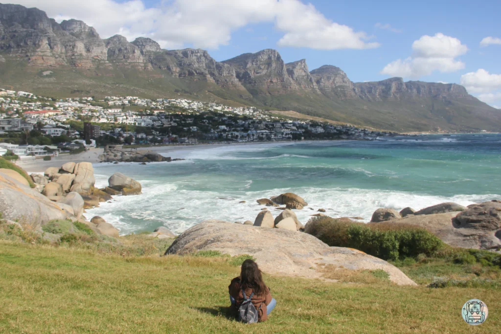 Teresa sentada en la hierba contemplando la playa de Camps Bay y los picos de los Doce Apóstoles desde Maidens Cove