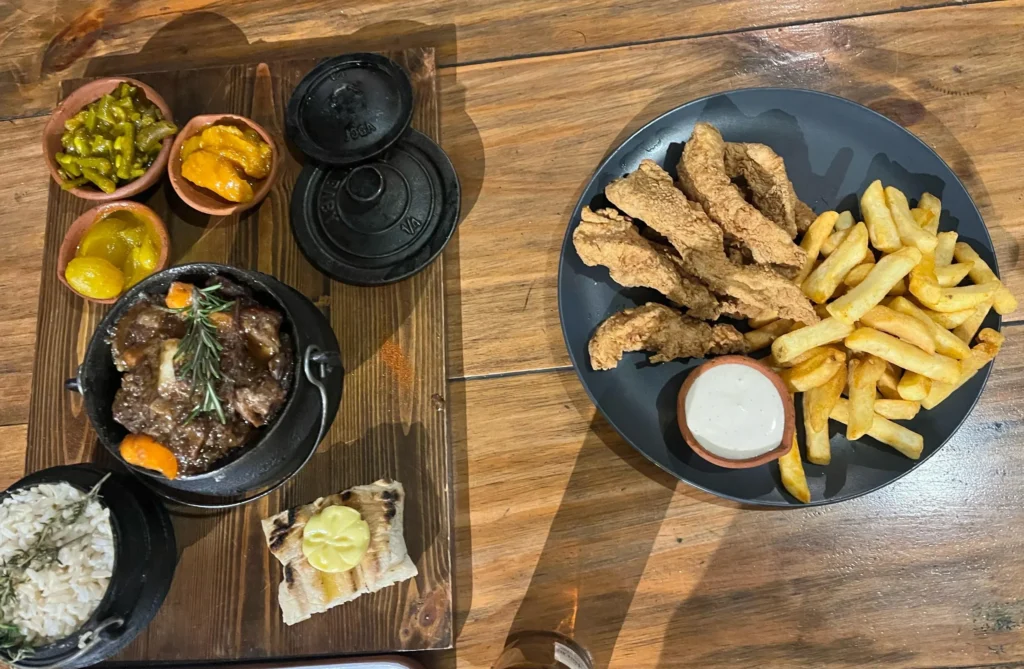 Platos de comida servidos sobre una mesa de madera con estofado en cazuela de hierro y tiras de pollo con patatas