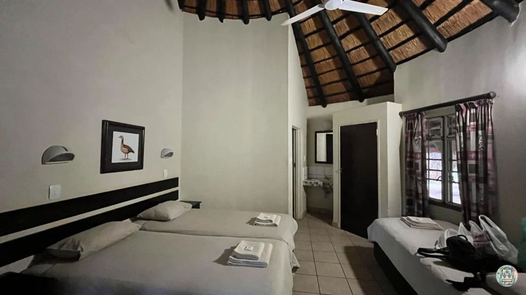 Interior de un bungalow con camas individuales y techo de paja tradicional en Crocodile Bridge