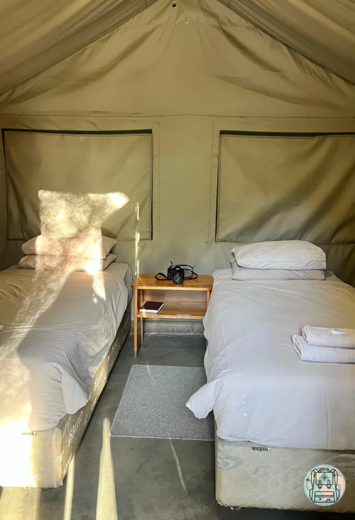 Interior de una tienda de safari con dos camas individuales y mesilla de noche en Skukuza